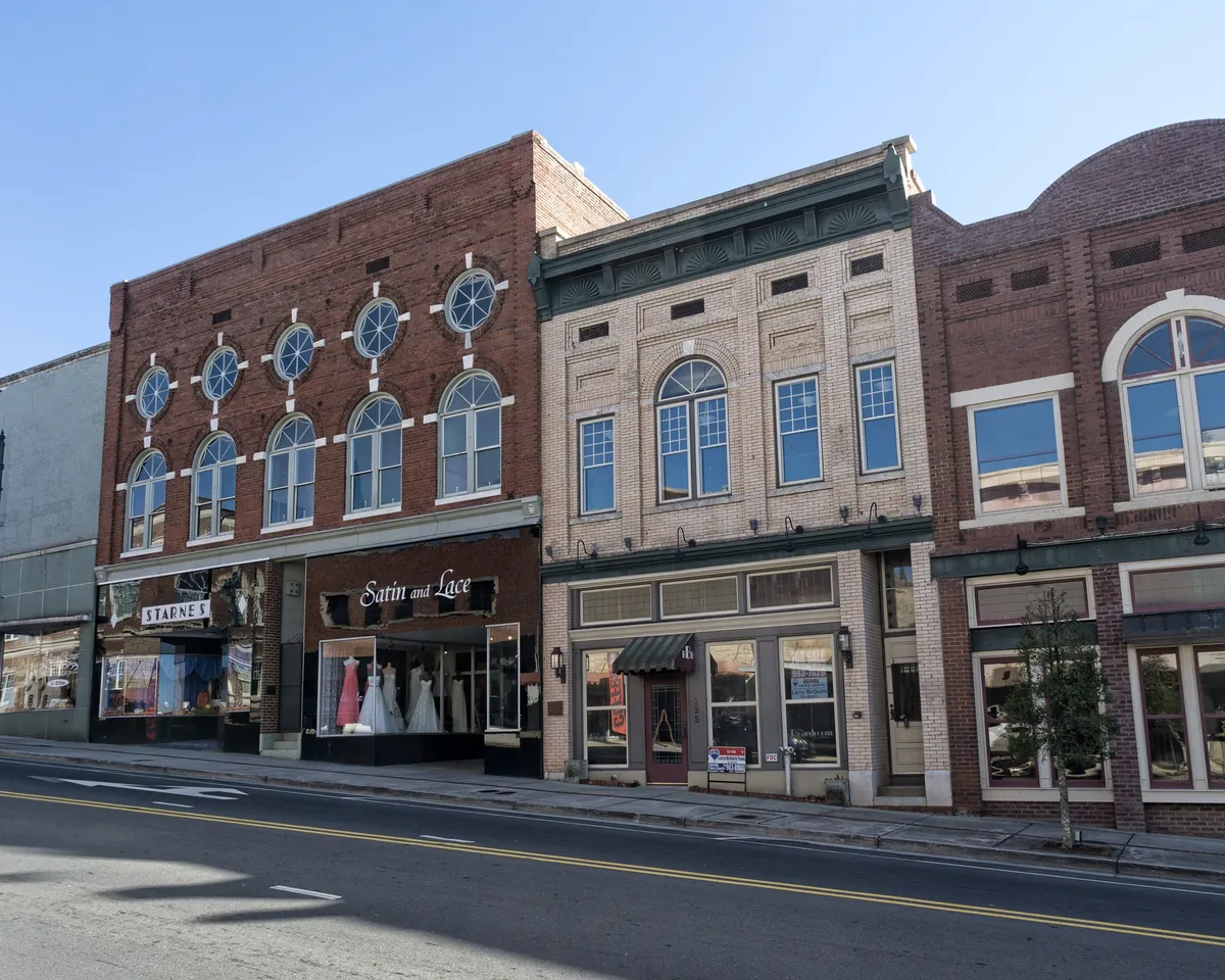 A row of restored brick and tan storefronts with arched upper windows along West Main Street in downtown Albemarle, North Carolina, under a clear blue sky